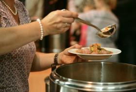 Person serving soup from large pan into bowl